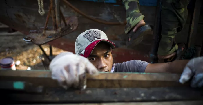 Young worker in a factory wearing gloves and a cap