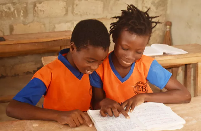 Two children in uniform read from a notebook 