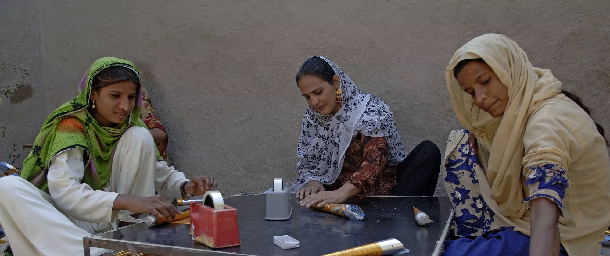 Three women sitting around a table rolling paper.