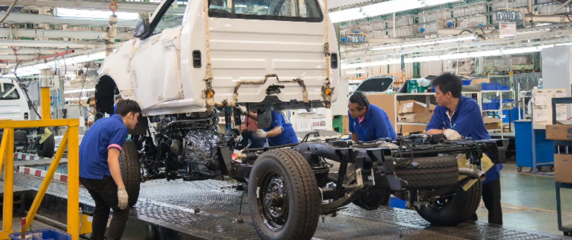 Workers assembling chassis of pickup cars, Thailand. 