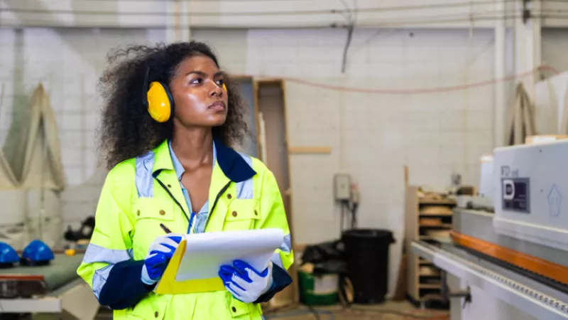 Women in protective equipment takes notes looking at machines in a factory