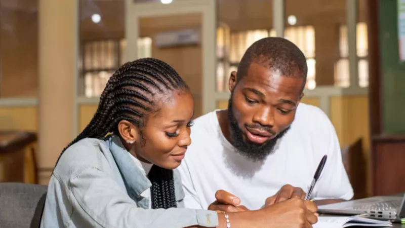 A young woman and a young man look together at a book and write something on it